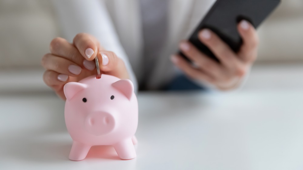 O fotografie cu cineva care pune schimbarea într-o pușculiță în timp ce ține un telefon mobil.