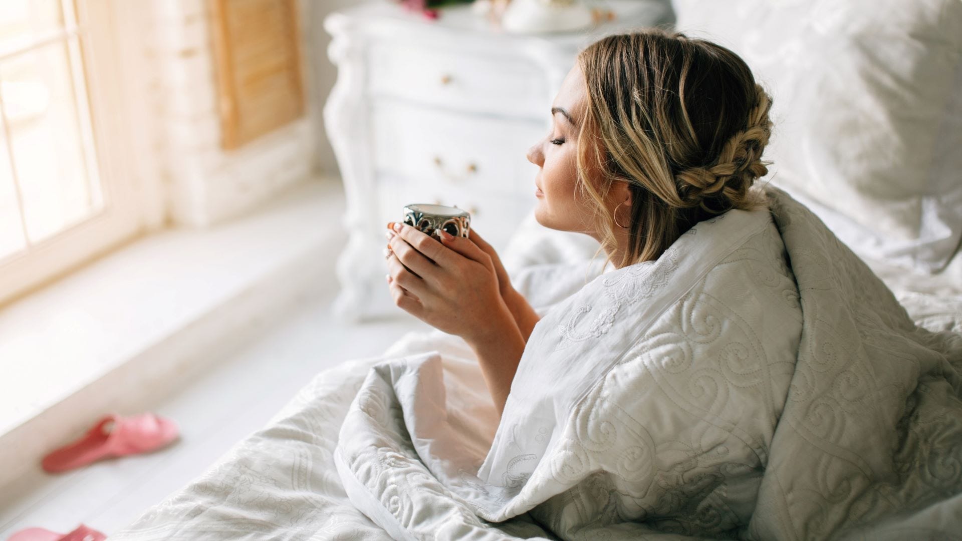 O femeie care bea cafea în pat dimineața.