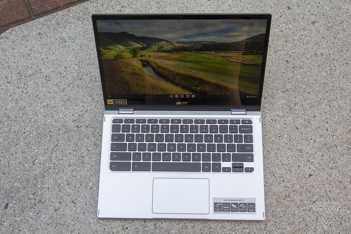 Chromebookul Acer Spin 513 pe o bancă de piatră, văzut de sus, deschis.  Ecranul afișează un peisaj pastoral.