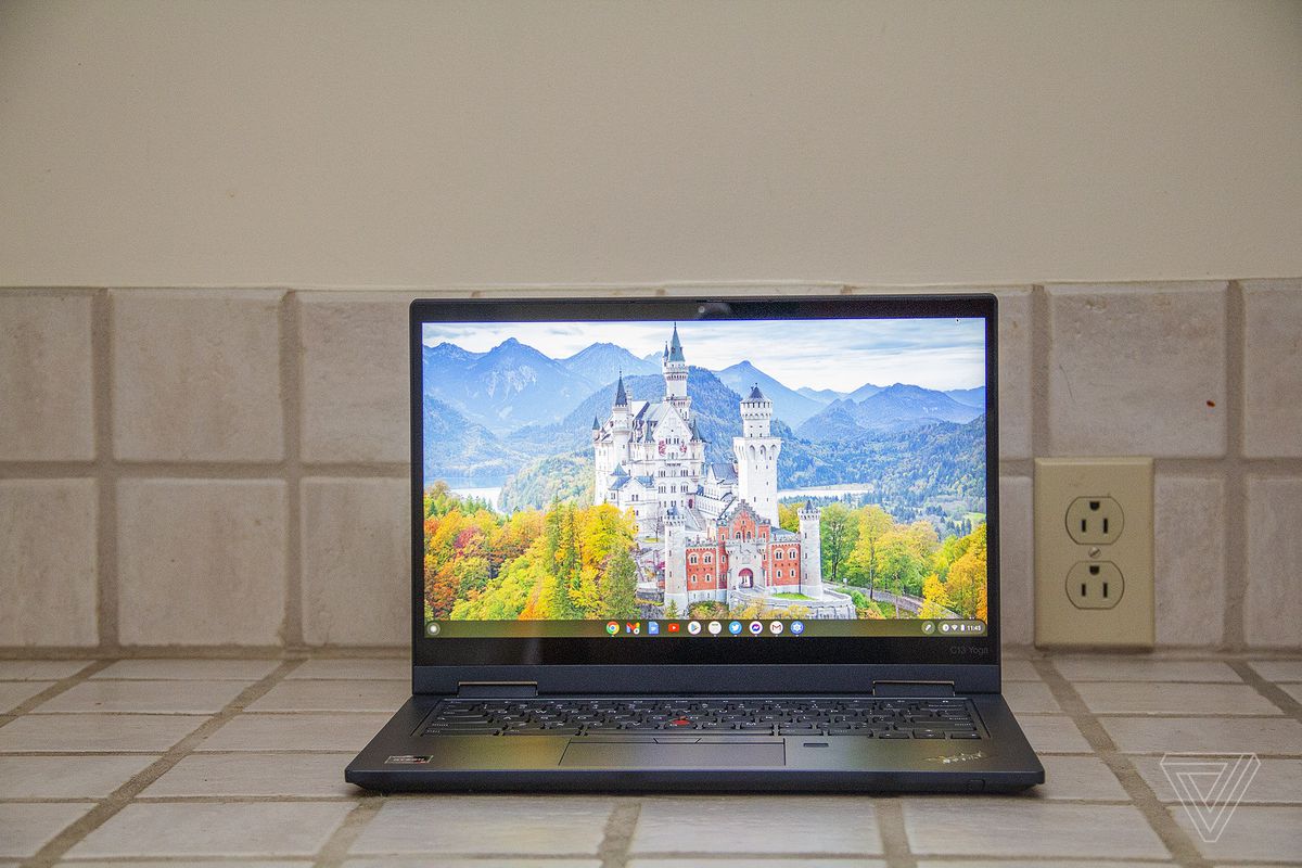 Chromebookul Lenovo ThinkPad C13 Yoga văzut din față pe un tejghea.  Ecranul afișează un castel alb înconjurat de copaci cu munți în fundal.