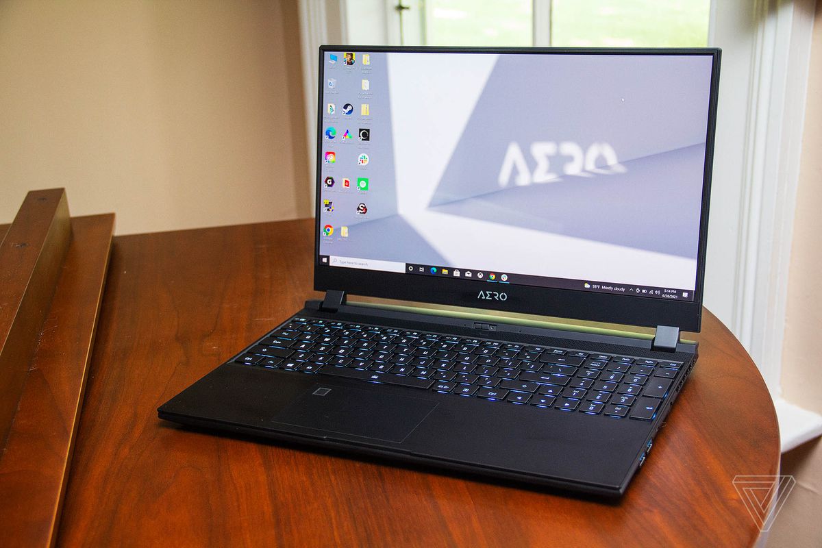 Gigabyte Aero 15 OLED se deschide pe un pian văzut de sus, înclinat spre stânga.  Tastatura este aprinsă în albastru deschis.  Ecranul afișează un desktop cu un fundal gri și alb.