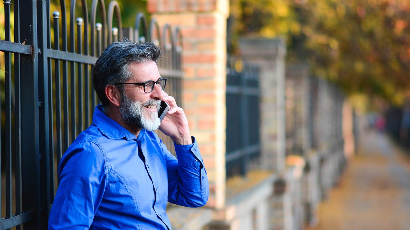 Un bărbat rezemat de un gard de fier, în timp ce vorbea la telefon.