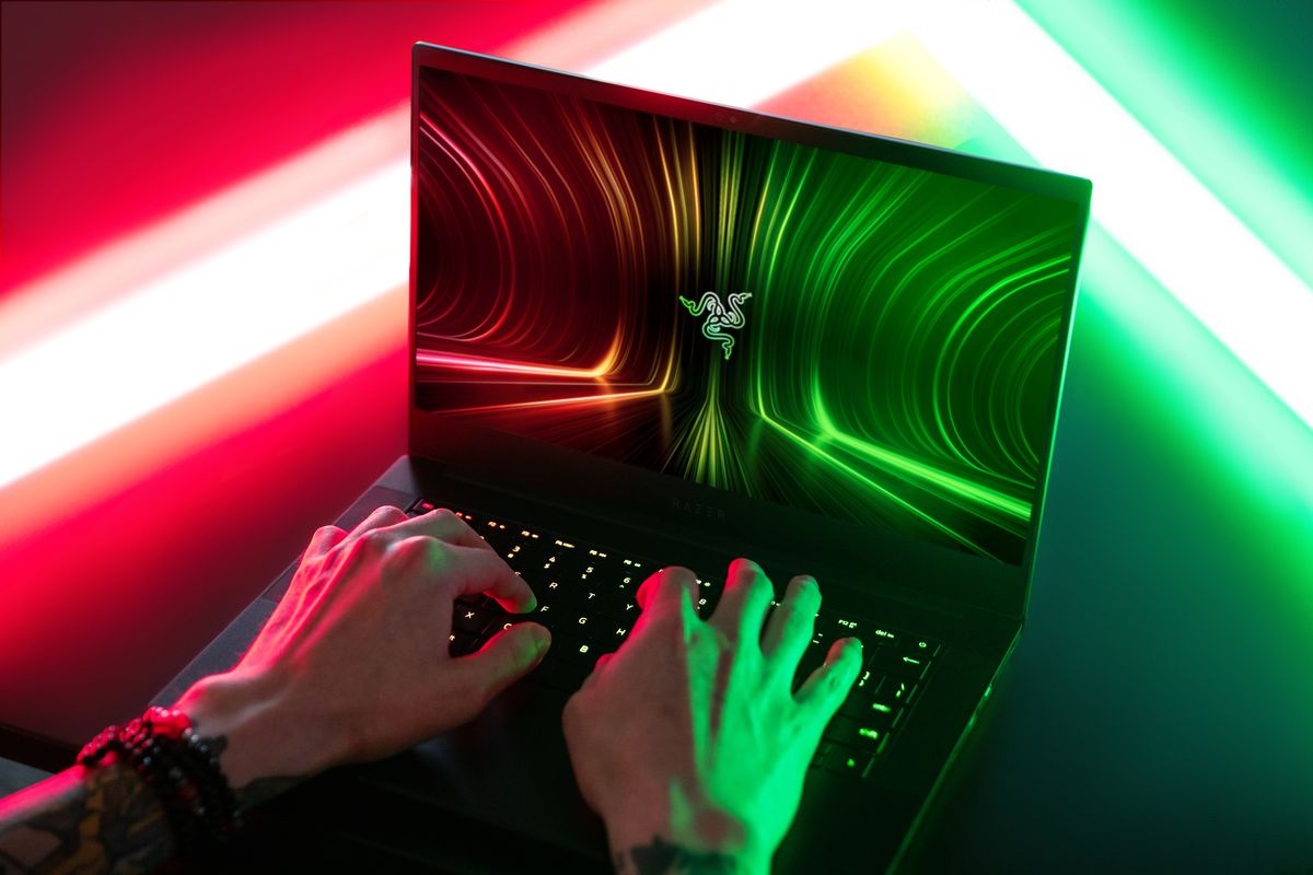 O fotografie peste umăr a unui utilizator tastând pe Razer Blade 14. Ecranul afișează sigla Razer pe un fundal roșu, verde și negru.