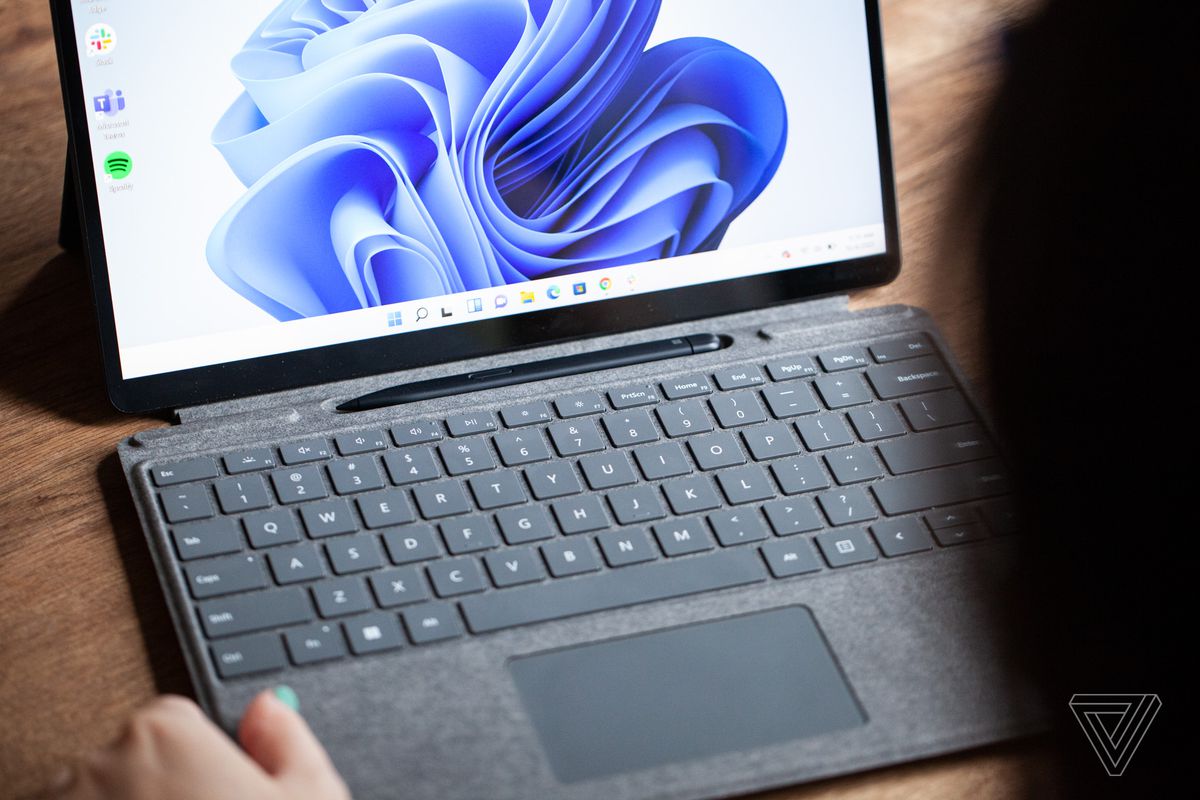 Surface Pro 8 este deschis, de aproape, cu tastatura scoasă și stiloul vizibil.  Ecranul afișează un vârtej albastru pe un fundal alb.