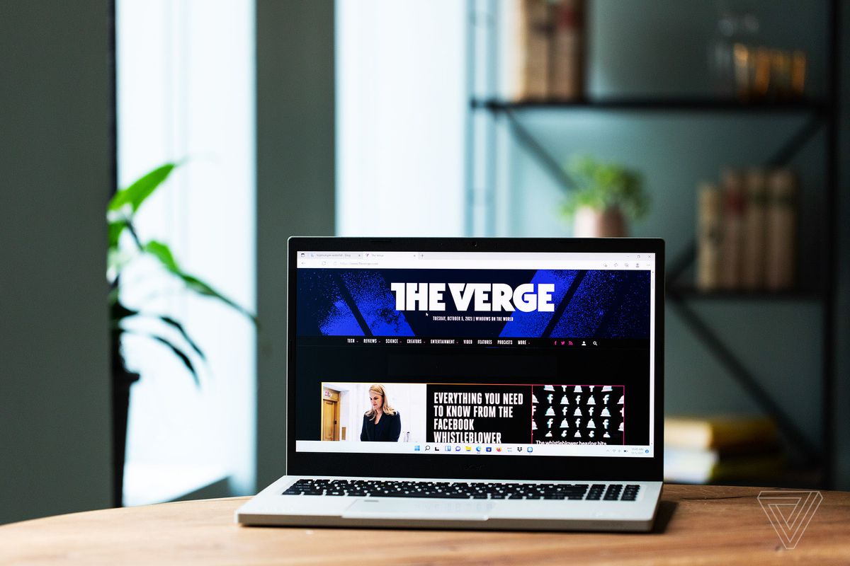 Acer Aspire Vero se deschide pe o masă de lemn cu un raft cu cărți în fundal.  Ecranul afișează pagina de pornire The Verge.