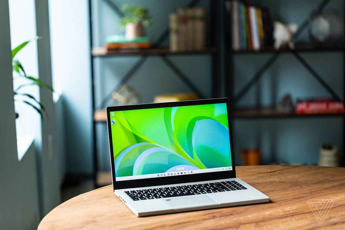 Acer Aspire Vero se deschide înclinat spre dreapta pe o masă de lemn cu un raft în fundal.  Ecranul afișează un fundal verde și albastru pentru desktop.